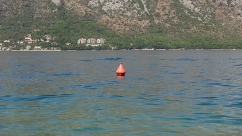 A bright orange conical buoy bobs on calm blue water as small waves shimmer. Red Stock Footage 329411842