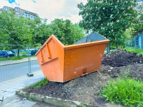 Bright orange dumpster is tilted on a pile of dirt near a construction site.. Stock Photos