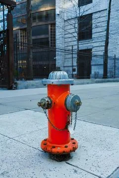 Bright orange fire hydrant on city sidewalk with buildings Stock Photos
