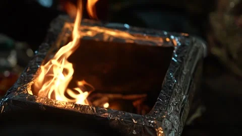 Bright orange flames flicker inside a square metallic ritual fire pit Stock Footage 335270743