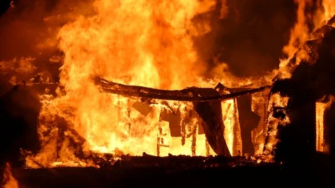 Bright orange flames ripping through structure with pieces of debris falling Video stock 115013463