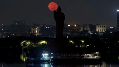 Bright orange full moon set behind buddha statue at hussain sagar lake in Stock Footage 255321832
