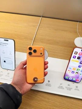 Bright orange iPhone 17 Pro on display held in hand at store with other iPh.. Stock Photos