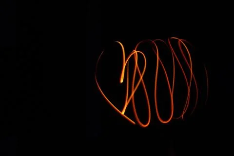Bright orange light trails creating abstract shapes in dark background Foto stock