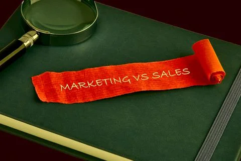 Bright orange paper scroll featuring the words Marketing vs Sales sits on a d Stock-Fotos