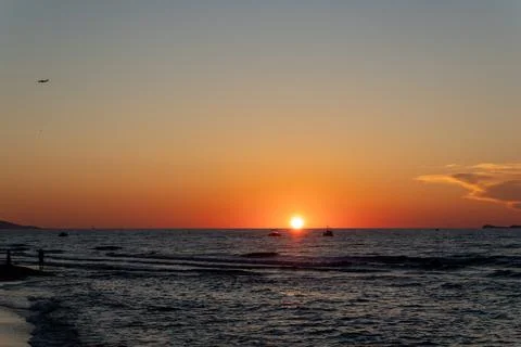 Bright orange sun sets on ocean horizon line with distant boats Stock-Fotos