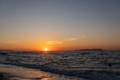 Bright orange sun setting on ocean horizon line at dusk Fotos Stock