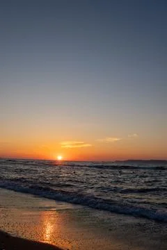 Bright orange sun setting over dark sea waves with wet sand reflection Stock-Fotos