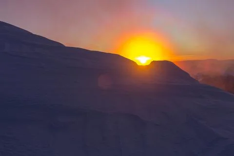 Bright orange sunrise of the sun disk in the snowy mountains Stock Photos