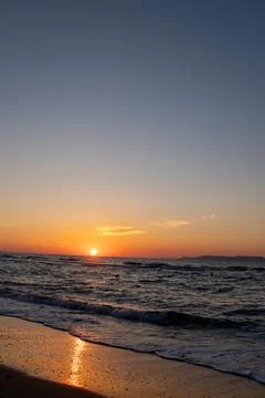 Bright orange sunset over dark ocean waves with reflection on wet shore Fotos Stock