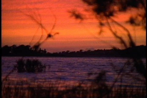 Bright orange sunset sky over lake. Camera tilts down to ripples on the water. Stock Footage 86752270