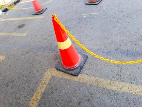 Bright orange traffic cones connected by a yellow plastic chain on asphalt. Stock Photos