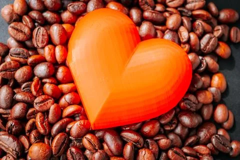 A bright orange translucent heart placed on roasted coffee beans. Stockfoto's