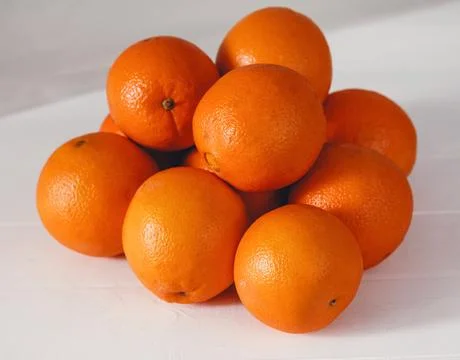 Bright oranges piled on white surface. Smooth texture with natural dimples. Stock Photos