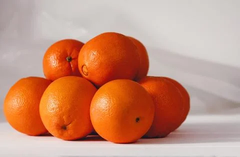 Bright oranges piled on white surface. Smooth texture with natural dimples. Stock Photos