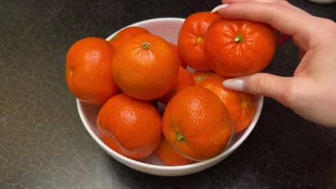 Bright oranges tangerines stand in a white plate on a black table a hand picks Stock Footage 301532778