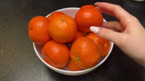 Bright oranges tangerines stand in a white plate on a black table a hand picks Stock Footage 301532996