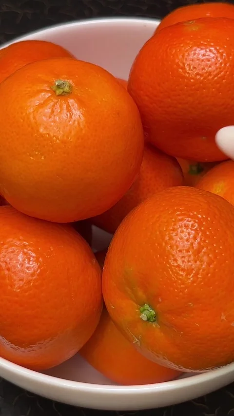 Bright oranges tangerines stand in a white plate on a black table a hand picks Stock Footage 303490833