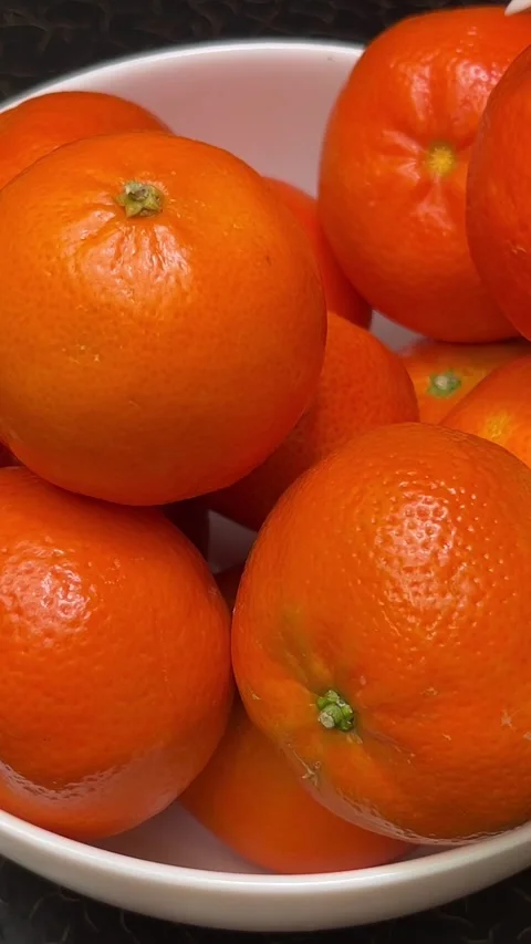 Bright oranges tangerines stand in a white plate on a black table a hand picks Stock Footage 313379672