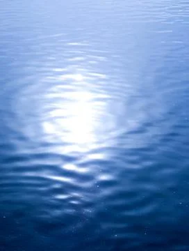 Bright patch of sun reflecting off calm blue water Stock Photos