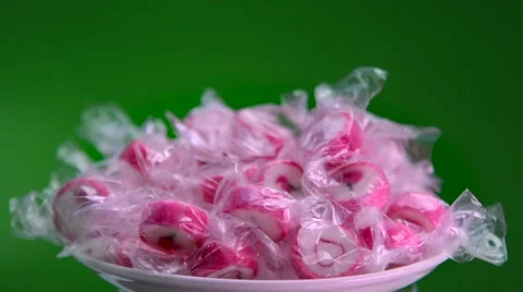 Bright pink candy in a transparent wrapper on a green background rotate slowly Stock Footage 62753872