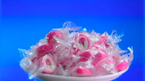 Bright pink candy in a transparent wrapper on a blue background rotate slowly. Stock Footage 62799224