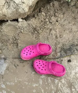 Bright Pink Clogs on Muddy Terrain with Textured Earth and Rock Stock Photos