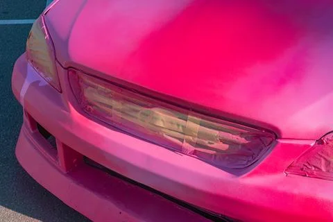 Bright pink compact car, angled in a concrete setting, midday lighting, scrat Stock Photos