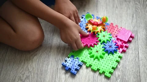 Bright plastic gear set arranged on floor while boy builds mechanism by hand. Video stock 330156182