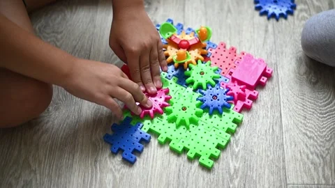Bright plastic gear set arranged on floor while boy builds mechanism by hand. Video stock 337533149