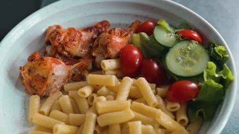 A bright plate features cooked chicken pieces alongside pasta and an assortment Video stock 338290533