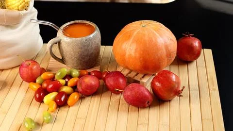 Bright pumpkin beverage inside ceramic mug beside large pumpkin, fruits Stock Photos