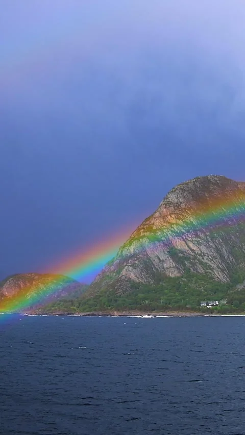 Bright rainbow arches over a lush mountain island in a Norwegian fjord Stock Footage 313173288