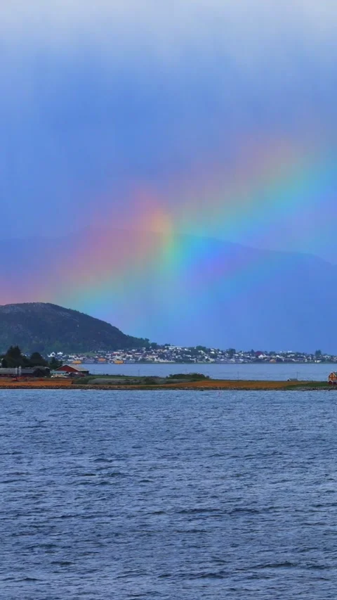 Bright rainbow arches over a lush mountain island in a Norwegian fjord Stock Footage 313173296