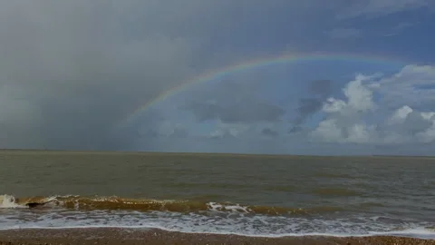 Bright rainbow arcs over a stormy green sea under heavy clouds on the horizon Stock Footage 324851078