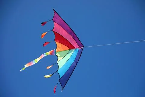 Bright rainbow colored kite flying high in the clear blue sky on a sunny day 库存照片