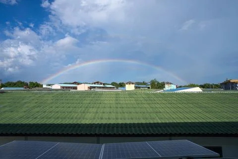 Bright rainbow over rooftops and solar panels. Natural beauty, climate, cle.. Stock Photos