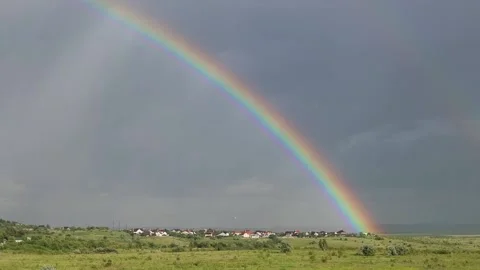 A bright rainbow rises from the meadow into the sky Stock Footage 205138347