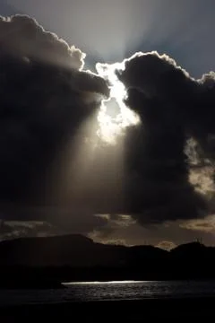 Bright rays of the sun shine trough dark clouds over lake Stock Photos