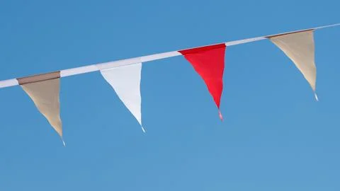 Bright red and white triangular flags hang against clear blue sky Stock Photos