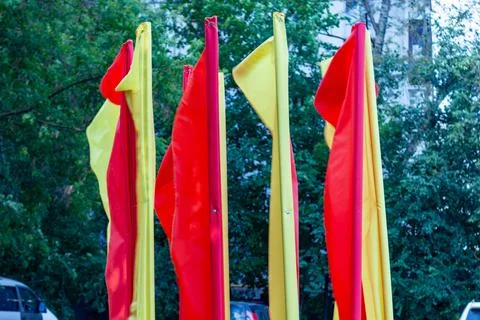 Bright red and yellow flags waving on poles against lush green trees background Stock Photos