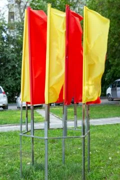 Bright red and yellow flags waving on metal poles in a green park Stock Photos