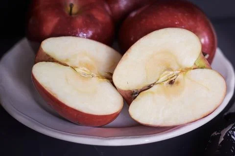 Bright red apples split in half in a white ceramic plate Stock Photos