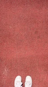Bright red athletic track surface with white sneakers standing on it during.. Stock Photos