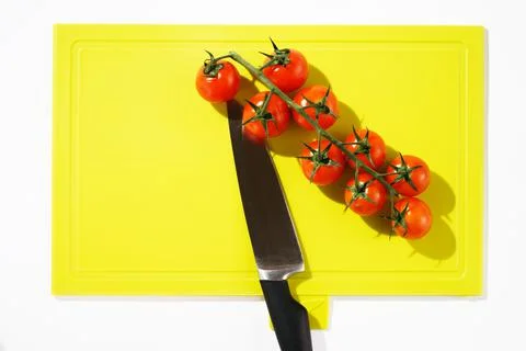 Bright red cherry tomatoes on white clean plastic cutting board with a kitchen Stock Photos