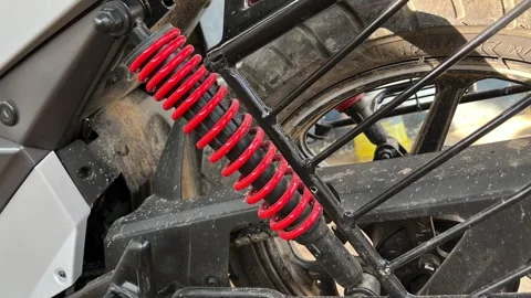 Bright red coil spring rear shock absorber on a dusty modern motorcycle Stockbeeldmateriaal 328409181