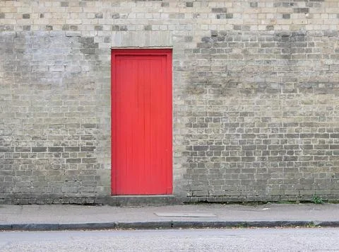 Bright red door embedded in grey brick wall with copy space Stock Photos