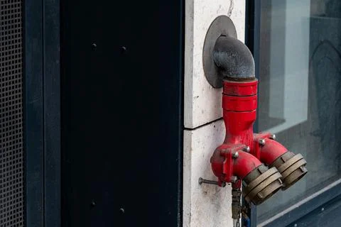 A bright red fire hydrant mounted on building exterior Stock Photos