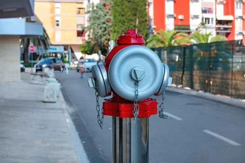 Bright red fire hydrant stands out on a sunny city street surrounded by gre.. Stock Photos