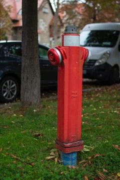 Bright red fire hydrant stands on a grassy area beside parked cars in an urban Stock Photos
